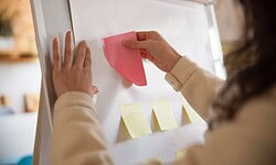 Persona colocando notas adhesivas en pizarra blanca.