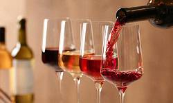 Vino tinto sirviendo en copa de cristal, con botella en primer plano y fondo difuminado.