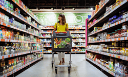 Imagen de una mujer comprando en supermercado con carrito lleno de productos en pasillo de alimentos.